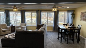 A living room with a sectional sofa, two armchairs, a dining table with chairs, and a ceiling fan.