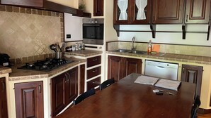 Una cocina con una mesa de madera, armarios, estufa y lavavajillas.