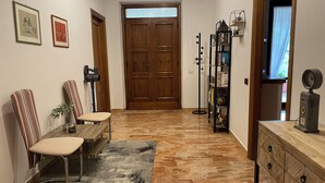 Un pasillo con una puerta de madera, un banco, una silla, una estantería y una pequeña mesa con un florero.