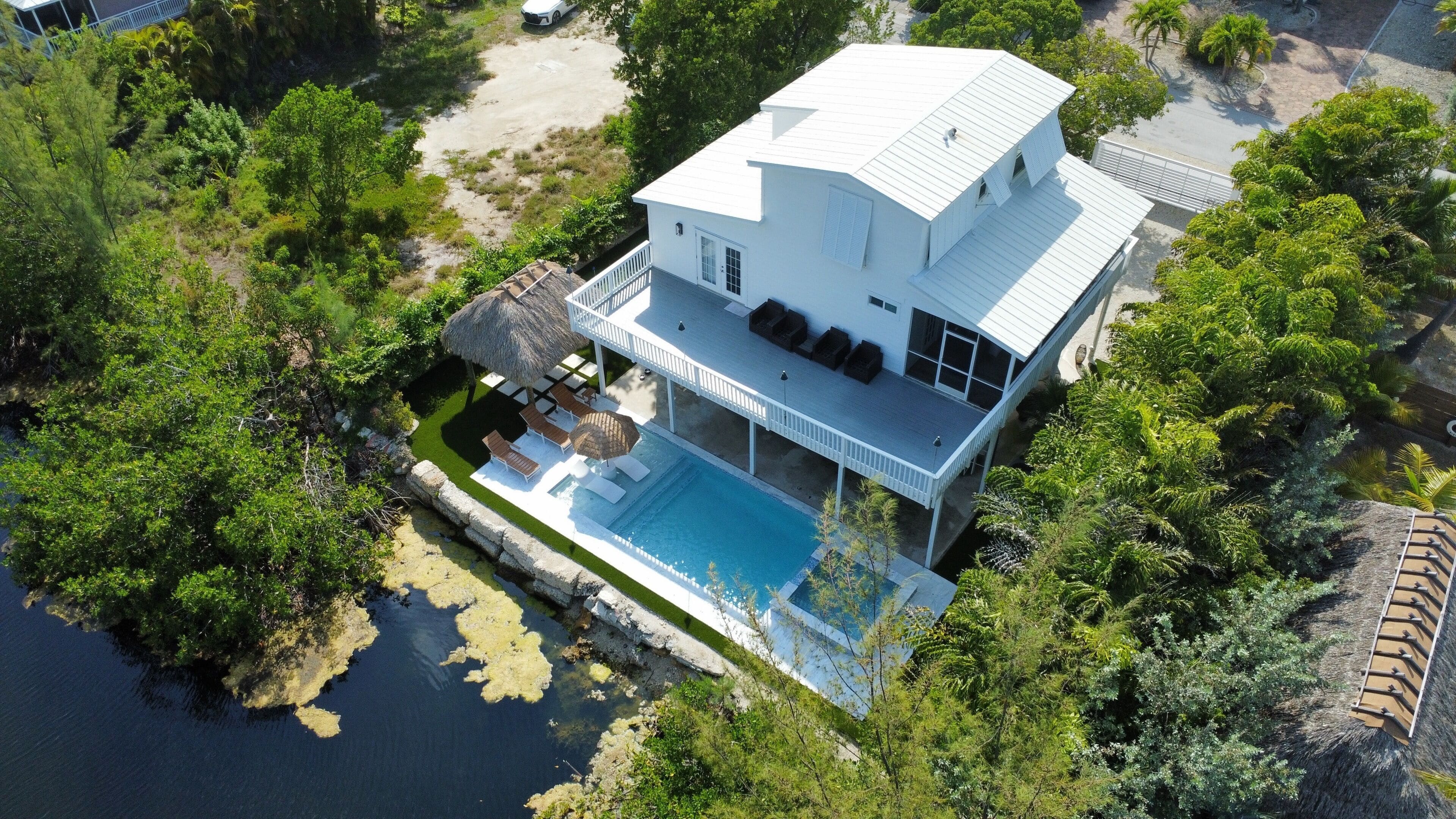 Une maison à deux étages avec une piscine, entourée d’une végétation luxuriante et dotée d’un quai.