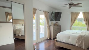 Un dormitorio con cama, televisión, ventilador de techo, cómoda y puerta corrediza de vidrio que da a un área exterior.