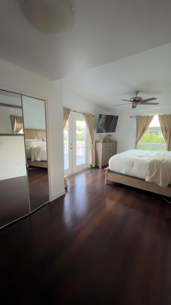 Een slaapkamer met een bed, een televisie, een plafondventilator, een dressoir en een schuifdeur die leidt naar een buitenruimte.