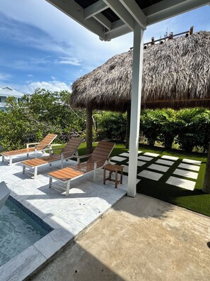 A poolside area with lounge chairs, a thatched roof structure, and a well-maintained garden.
