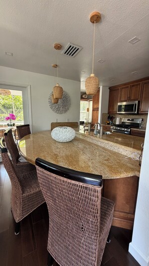 A kitchen with a large island, wicker chairs, and pendant lights.