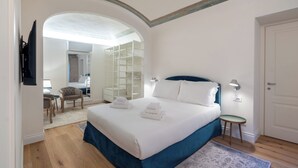 Un dormitorio con una cama grande, un vestidor, un escritorio con silla y vistas por un arco.