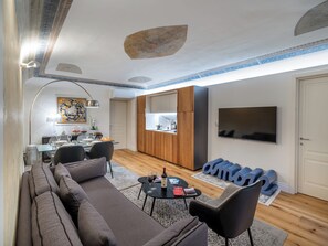 A modern living room with a sofa, a dining area with a table and chairs, a kitchen area with cabinets, and a TV mounted on the wall. - Palazzo Nori elegant & renovated apartment in the hearth of Florence (Firenze)