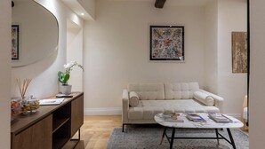 Una sala moderna con un sofá color beige, una mesa de centro, una consola de madera con una orquídea en maceta y un espejo grande.