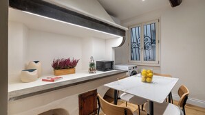 Una cocina moderna con encimera blanca, microondas integrado y una ventana con rejas decorativas de hierro.