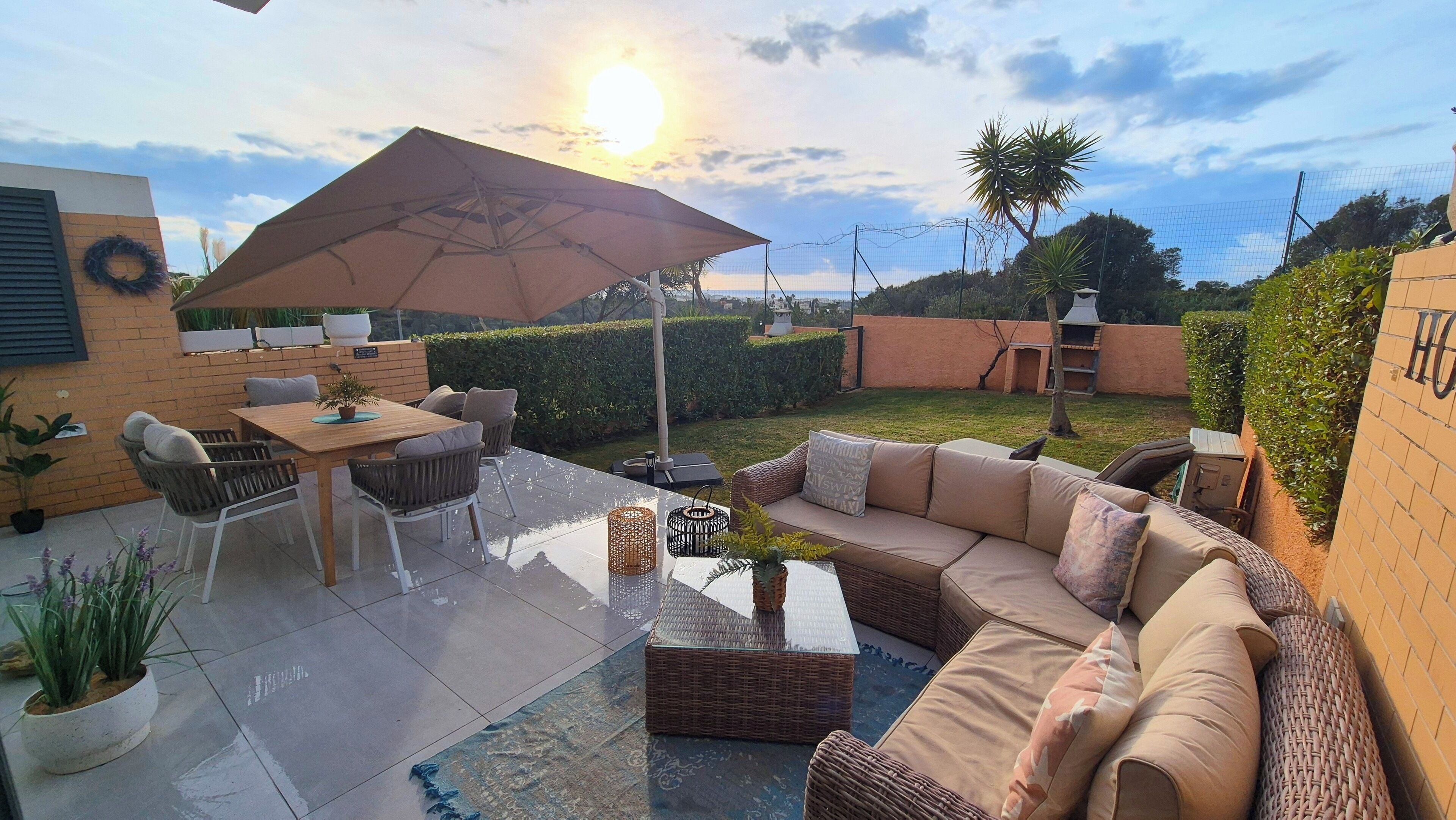 An outdoor patio with a table and chairs, a wicker sofa, and a large umbrella.
