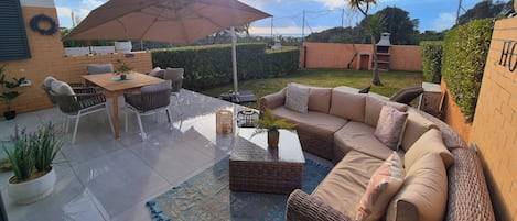 An outdoor patio with a table and chairs, a wicker sofa, and a large umbrella.