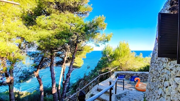 A stone building with a balcony overlooking a coastal area with trees and a clear blue sea. - Charming stone trullo with sea access (house F) (Castro)