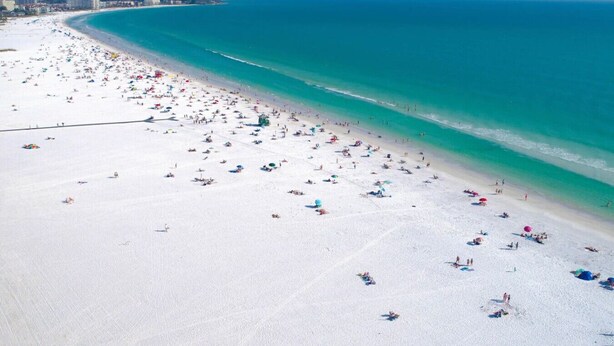 Ampia spiaggia con numerosi ombrelloni e lettini, un mare cristallino e una costa lontana con edifici.