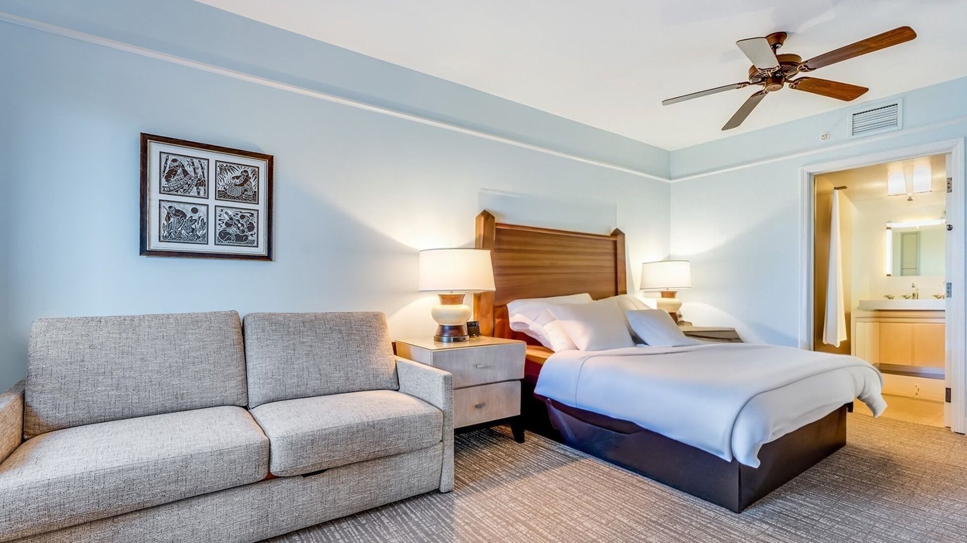 Une chambre d’hôtel avec un lit, un canapé, un ventilateur de plafond et un tableau encadré au mur.