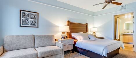 Une chambre d’hôtel avec un lit, un canapé, un ventilateur de plafond et un tableau encadré au mur.