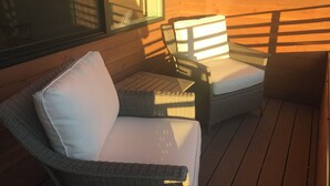 A wicker chair with a white cushion on a wooden deck, with sunlight casting shadows on the wall. - Your Bozeman Basecamp: Comfortable Condo in the Perfect Downtown Location (Bozeman)