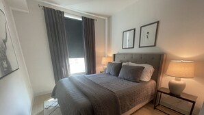 A bedroom with a bed, two bedside tables with lamps, a window with curtains, and two framed pictures on the wall. - Your Bozeman Basecamp: Comfortable Condo in the Perfect Downtown Location (Bozeman)
