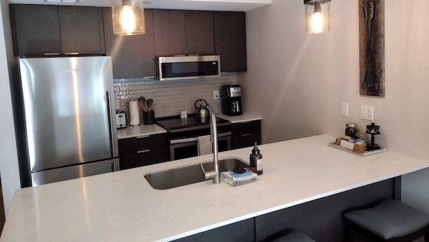 A modern kitchen with stainless steel appliances, a white countertop, and dark cabinetry. - Your Bozeman Basecamp: Comfortable Condo in the Perfect Downtown Location (Bozeman)