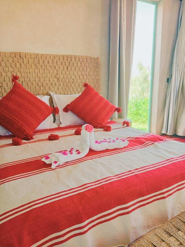 A hotel room with a bed, red and white striped bedspread, two red pillows, and a decorative swan made of towels.