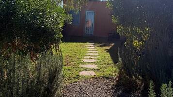 A pathway leading to a building with a blue door, surrounded by greenery and a clear sky.