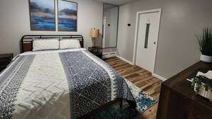 A bedroom with a bed, a bedside table, a lamp, a mirror, and a door. - Spacious Apartment in Horseheads, NY (Horseheads)