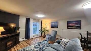 Un salon avec un canapé, un téléviseur, une lampe, une plante et une vue sur l’extérieur.