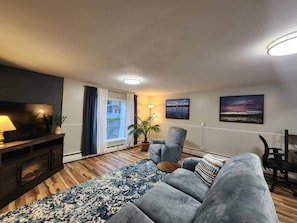 A living room with a sofa, a TV, a lamp, a plant, and a view of the outdoors. - Spacious Apartment in Horseheads, NY (Horseheads)