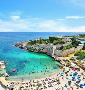 A coastal area with a beach, clear turquoise waters, and a fortified structure with greenery. - Deledda Vacation Home (Monopoli)