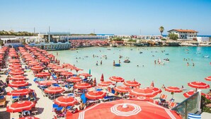 A beach with numerous red umbrellas and people swimming in the water.