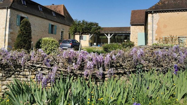 A stone building with a car parked in front, surrounded by purple flowers and greenery. - Renovated farmhouse with swimming pool and 3ha garden (Limeuil)