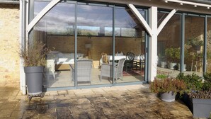 A covered patio with a glass enclosure, wicker furniture, and potted plants. - Renovated farmhouse with swimming pool and 3ha garden (Limeuil)