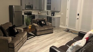 A compact living space with a kitchenette, grey cabinets, a refrigerator, a microwave, a stove, and a dining area.