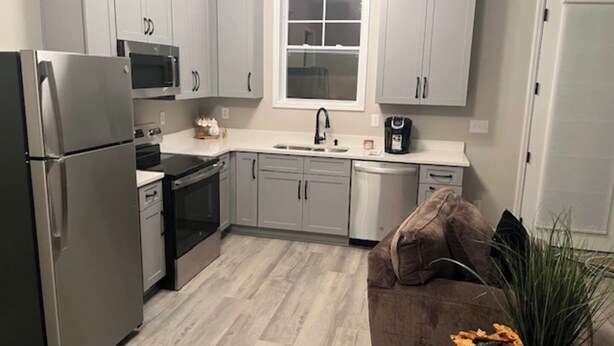 A modern kitchen with grey cabinets, stainless steel appliances, a window, and a brown couch with a plant.
