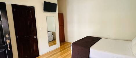 Quarto de hotel com cama, escrivaninha, cadeira, guarda-roupa e televisão.