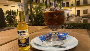 A table with a bottle of Corona Extra beer, a glass of a mixed drink with a garnish, and two boxes of GAMA salad dressing. - Hotel California Pacific Palm (Escuintla)
