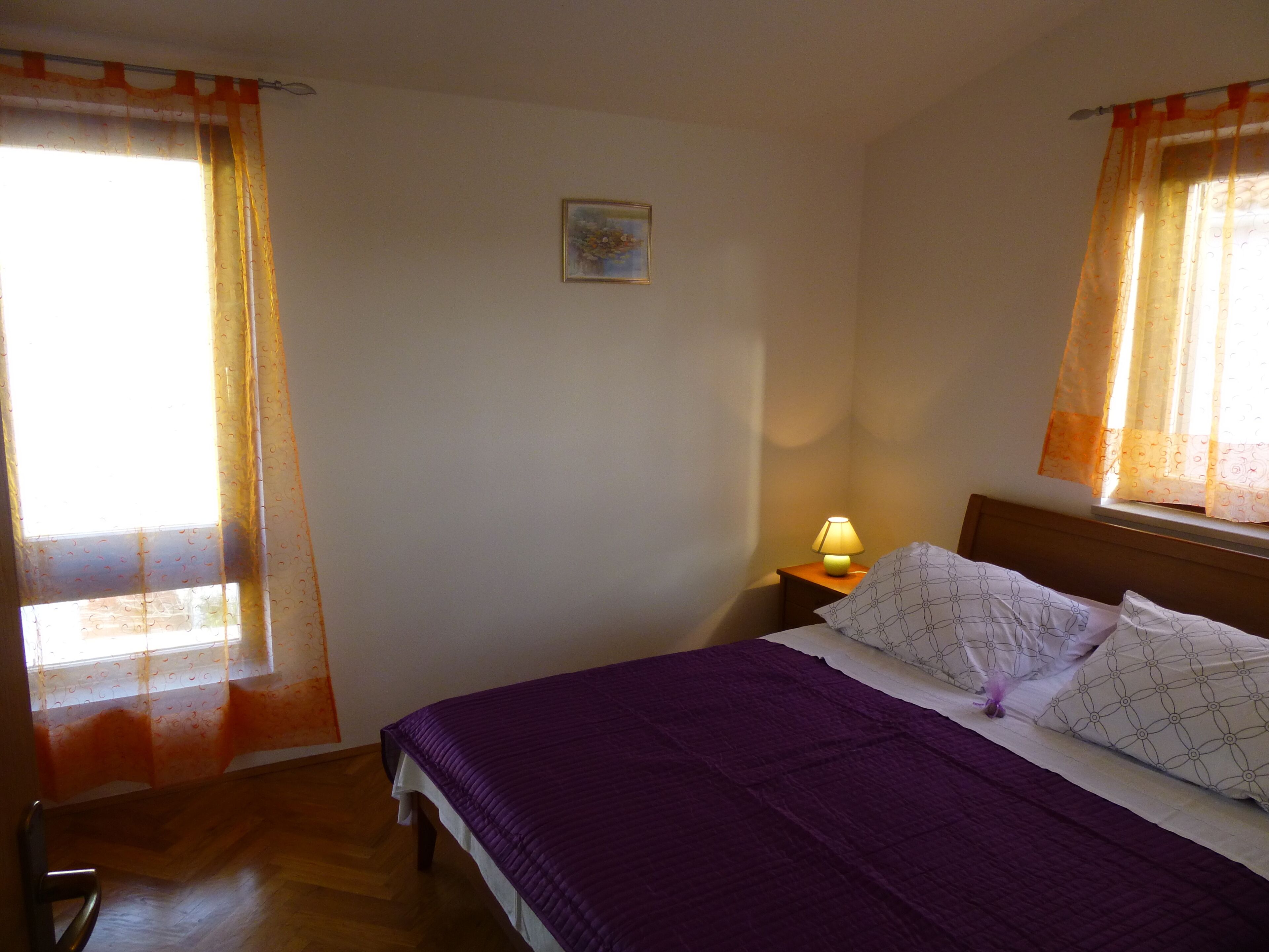A bedroom with a bed, a nightstand with a lamp, and a window with curtains.