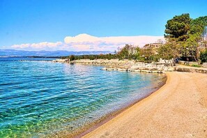 Una playa con agua cristalina, una orilla arenosa y montañas al fondo.
