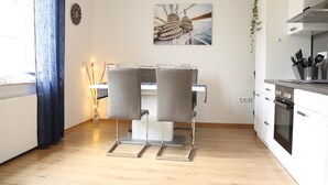 A modern kitchen with white cabinets, a built-in oven, and a dining area with two grey chairs and a table. - Cast off - maritime vacation home in the countryside (Krummhörn)