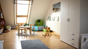 A child's playroom with a window, a table, chairs, a rocking chair, and a bookshelf. - Cast off - maritime vacation home in the countryside (Krummhörn)