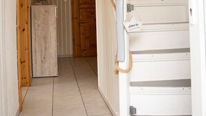 A narrow hallway with a wooden door at the end, a white staircase with a handrail, and a small refrigerator against the wall. - Cast off - maritime vacation home in the countryside (Krummhörn)