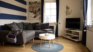 A living room with a grey sofa, a round coffee table, a TV on a stand, and nautical-themed decor. - Cast off - maritime vacation home in the countryside (Krummhörn)