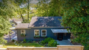 A two-story house with a dark exterior, a covered porch, and a small front yard with stepping stones and potted plants. - Historic Uptown Retreat in Hot Springs, Arkansas (Hot Springs)