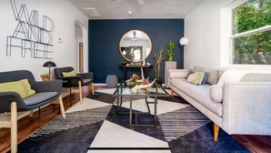 A modern living room with a dark blue accent wall, a round mirror, a glass coffee table, and two sofas. - Historic Uptown Retreat in Hot Springs, Arkansas (Hot Springs)