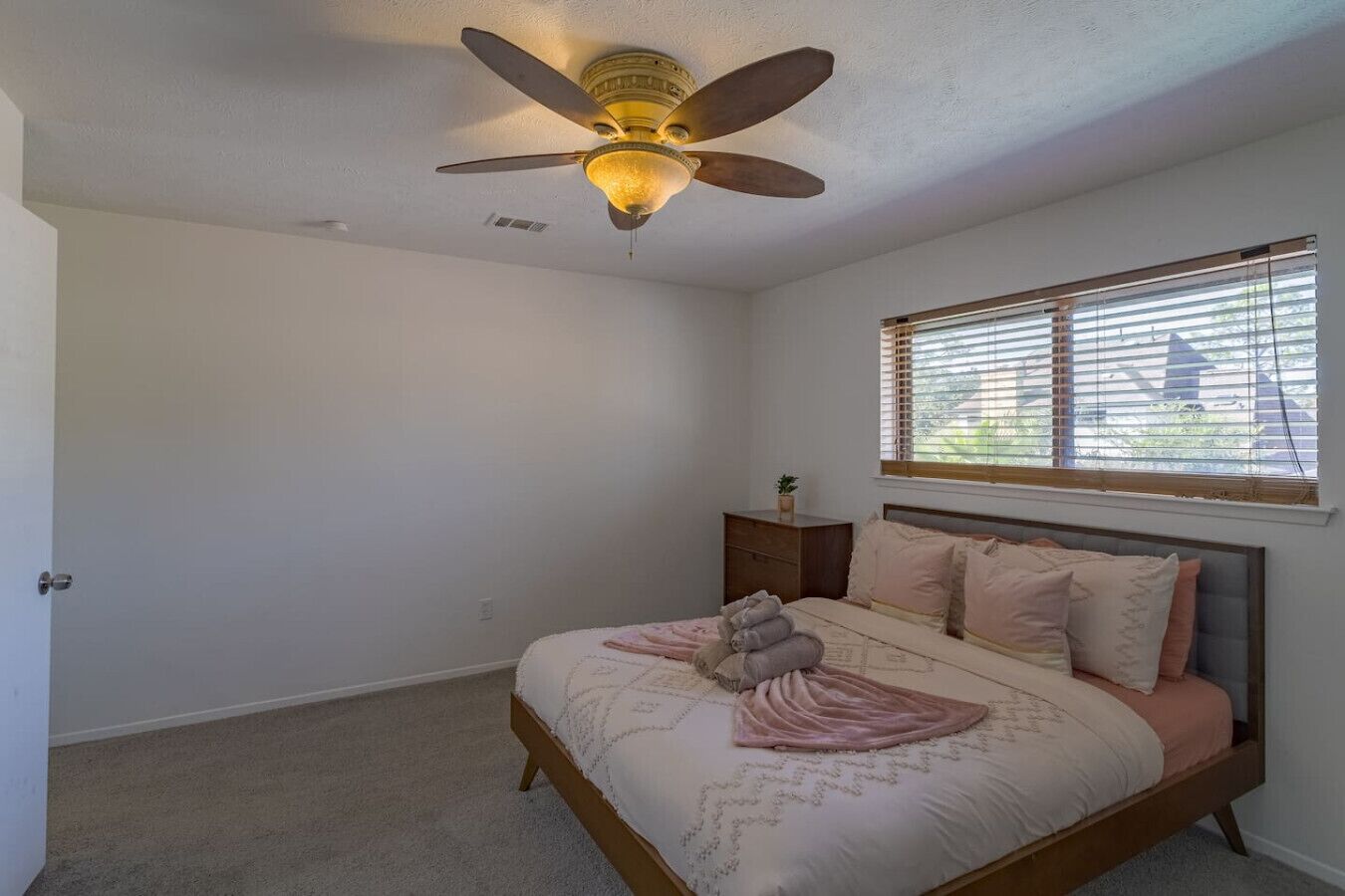 Une chambre à coucher avec un lit, une table de chevet, un ventilateur de plafond et une fenêtre avec des stores.