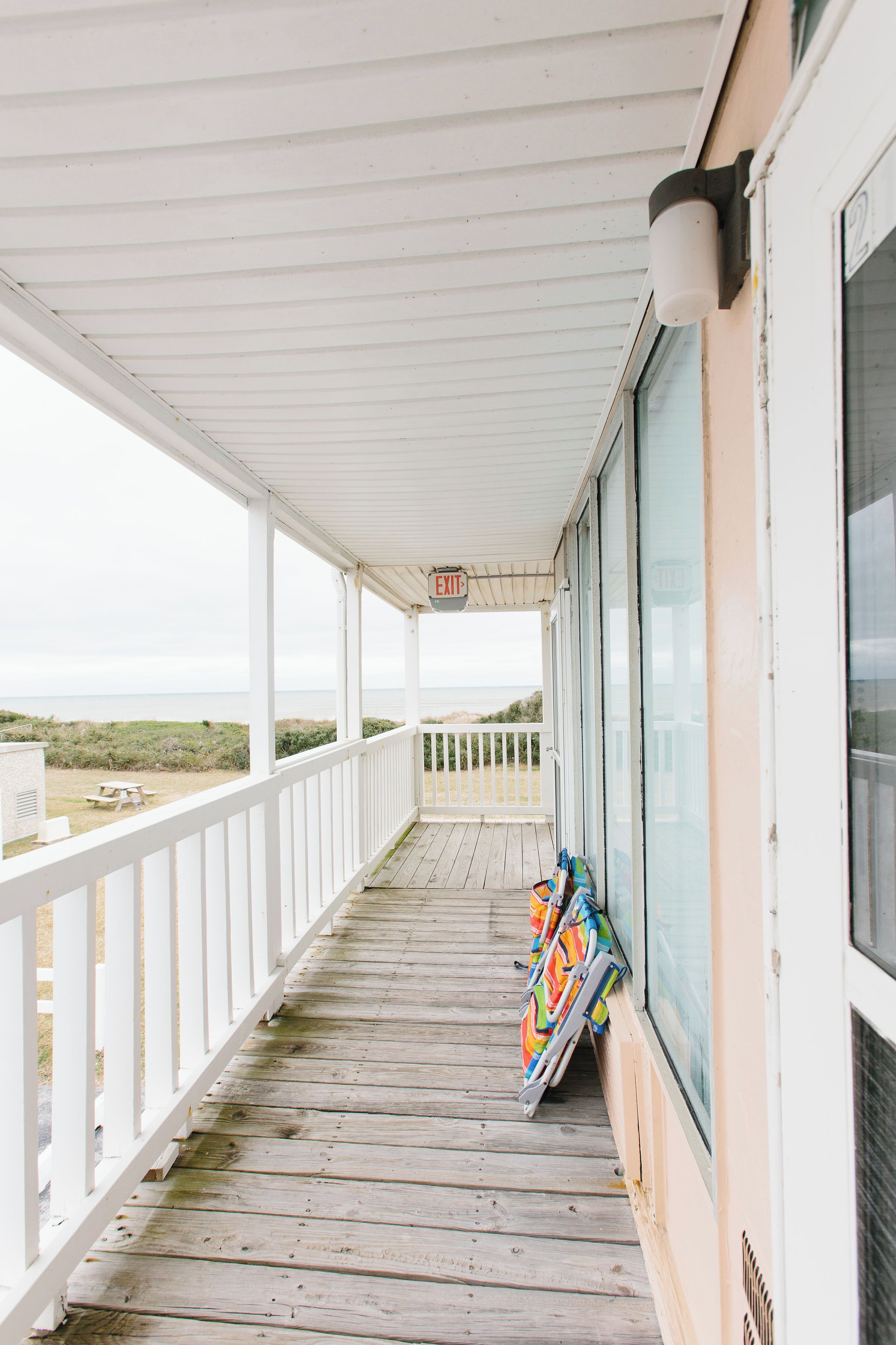 A covered porch with a view of the beach, a picnic table, and a row of colorful beach chairs.