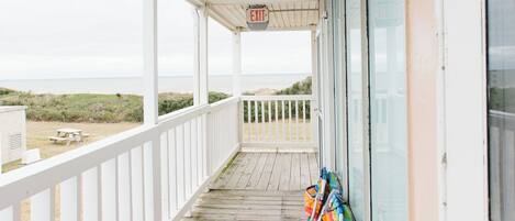 A covered porch with a view of the beach, a picnic table, and a row of colorful beach chairs.