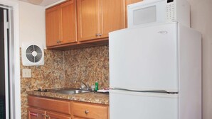 Una cocina con armarios de madera, encimera de granito, refrigerador blanco y microondas.