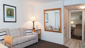 Una sala de estar con un sofá, una mesa, una lámpara, un espejo y una puerta que da a un dormitorio.