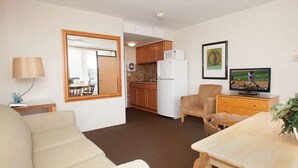 Un espacio habitable compacto con sofá, mesa de comedor, televisor, zona de cocina y un espejo grande.