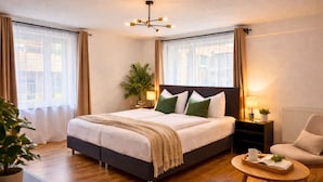 Ein Hotelzimmer mit Bett, Nachttischen, einem Sessel, einem kleinen Tisch mit Tablett und einer Topfpflanze.
