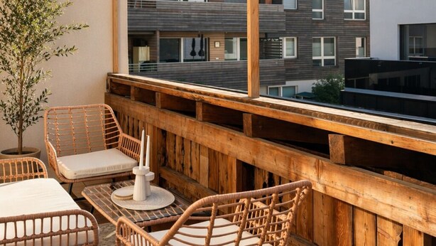 Ein Balkon mit Rattanmöbeln, einem Topfpflanzen und Blick auf ein mehrgeschossiges Gebäude.